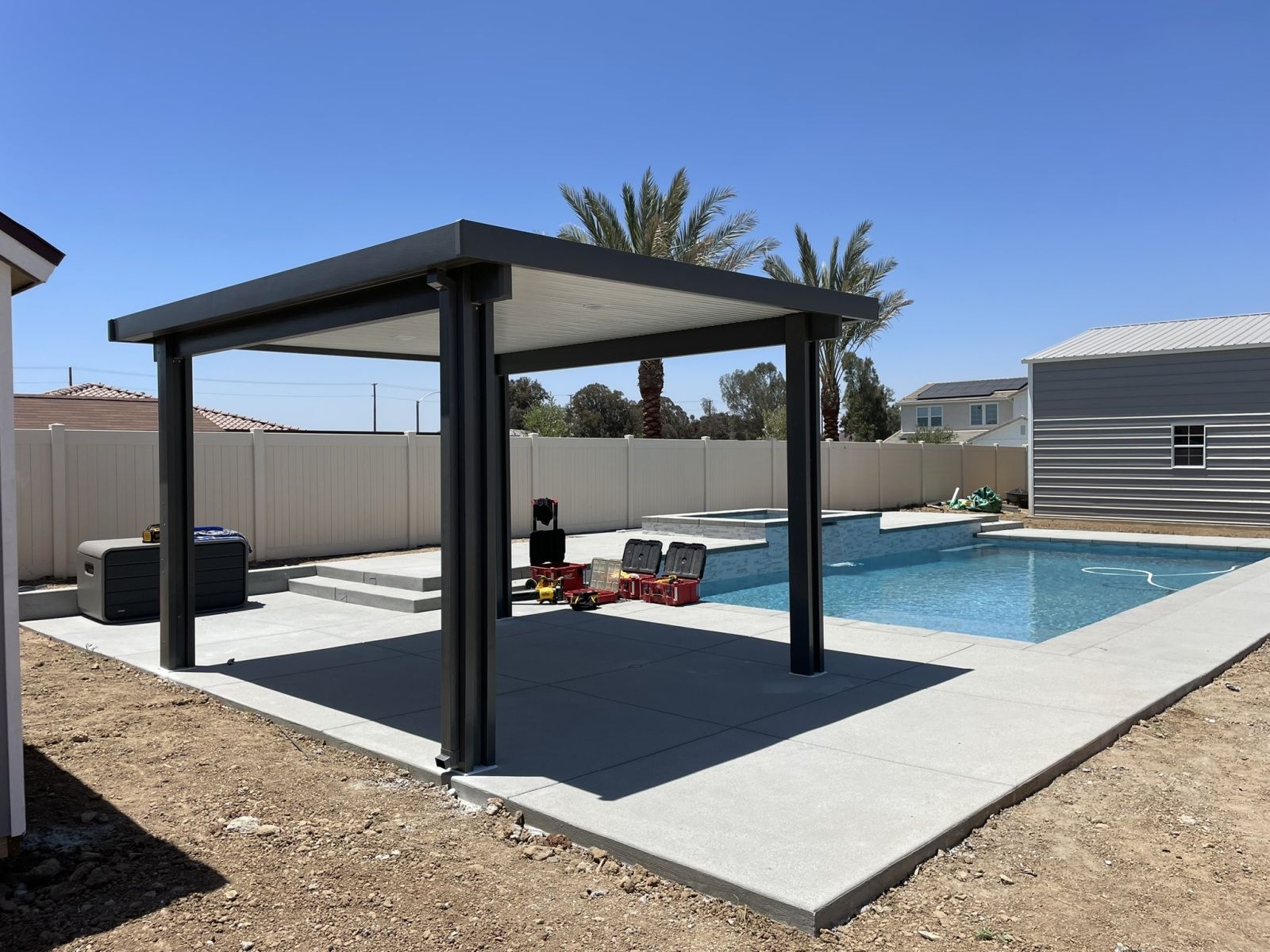 Pergola over a pool. Concrete patio. Gray pergola, blue pool. Boy playing with toys. Sunny day.