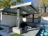 Modern outdoor kitchen with gray roof, built-in grill, seating, and pool.