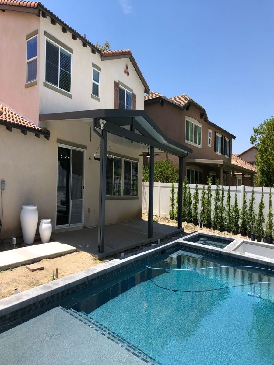 Backyard patio with pool, awning, and a two-story house with tan stucco and red tile roof.