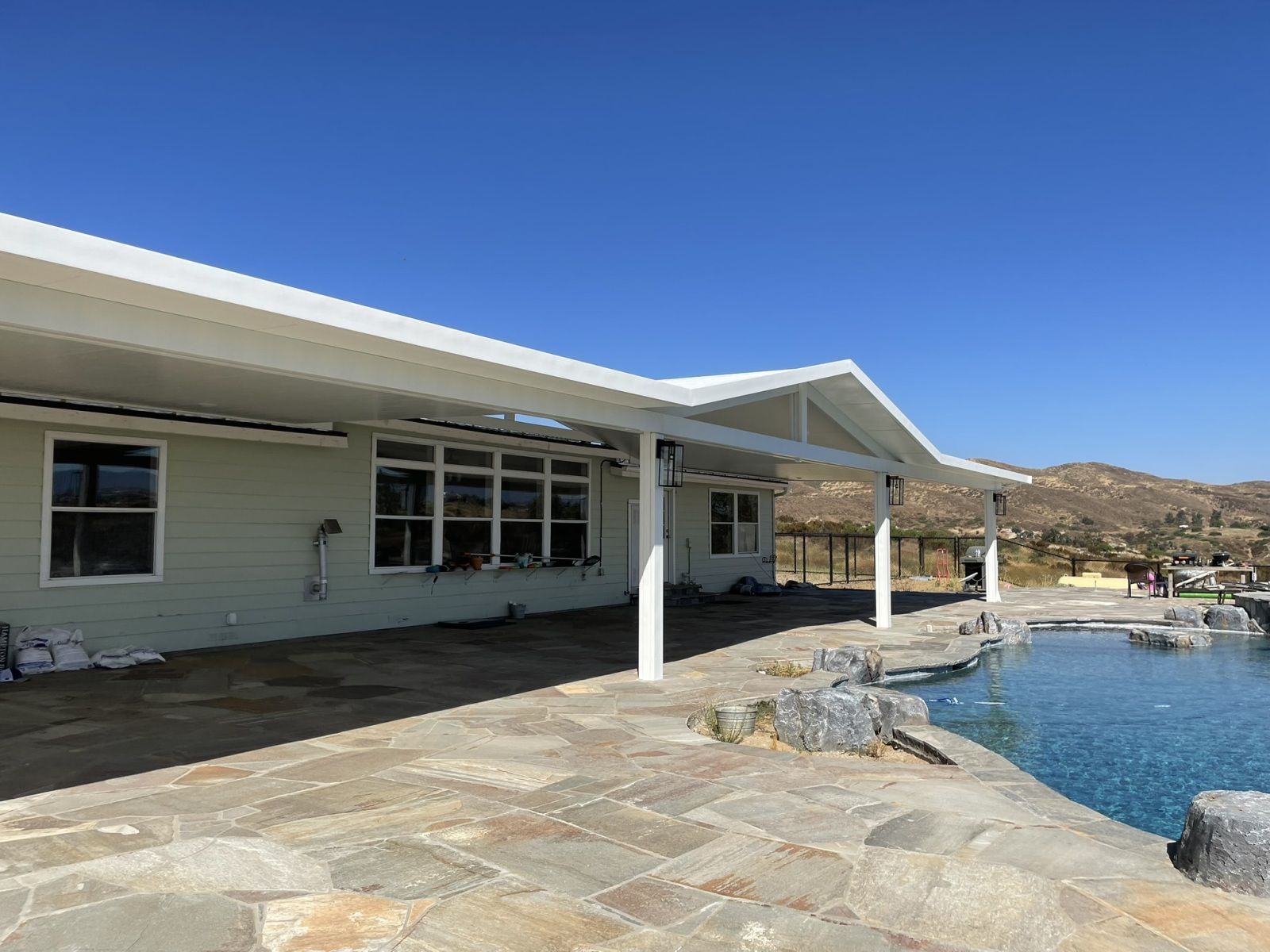 House with white roof and patio overlooking a pool on a sunny day.