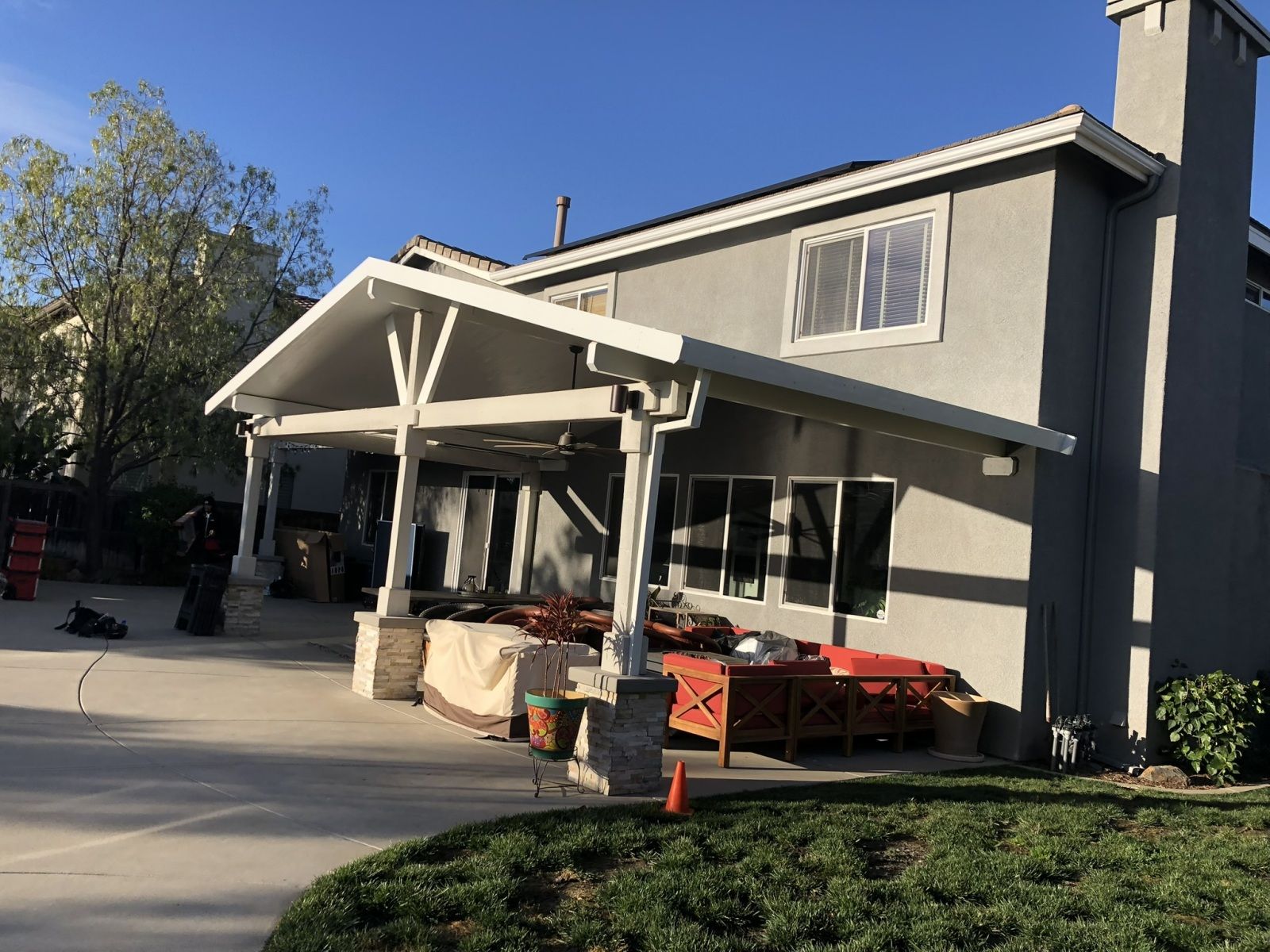 Covered patio attached to a two-story house with construction materials visible, on a sunny day.