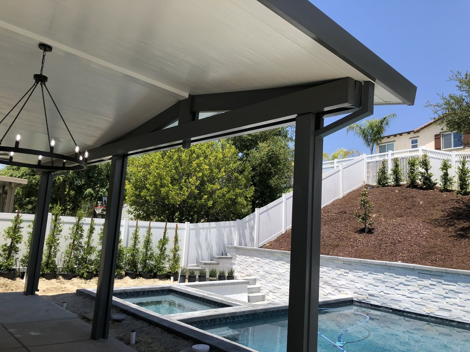 Covered patio overlooking a pool and yard, with gray beams and white ceiling.