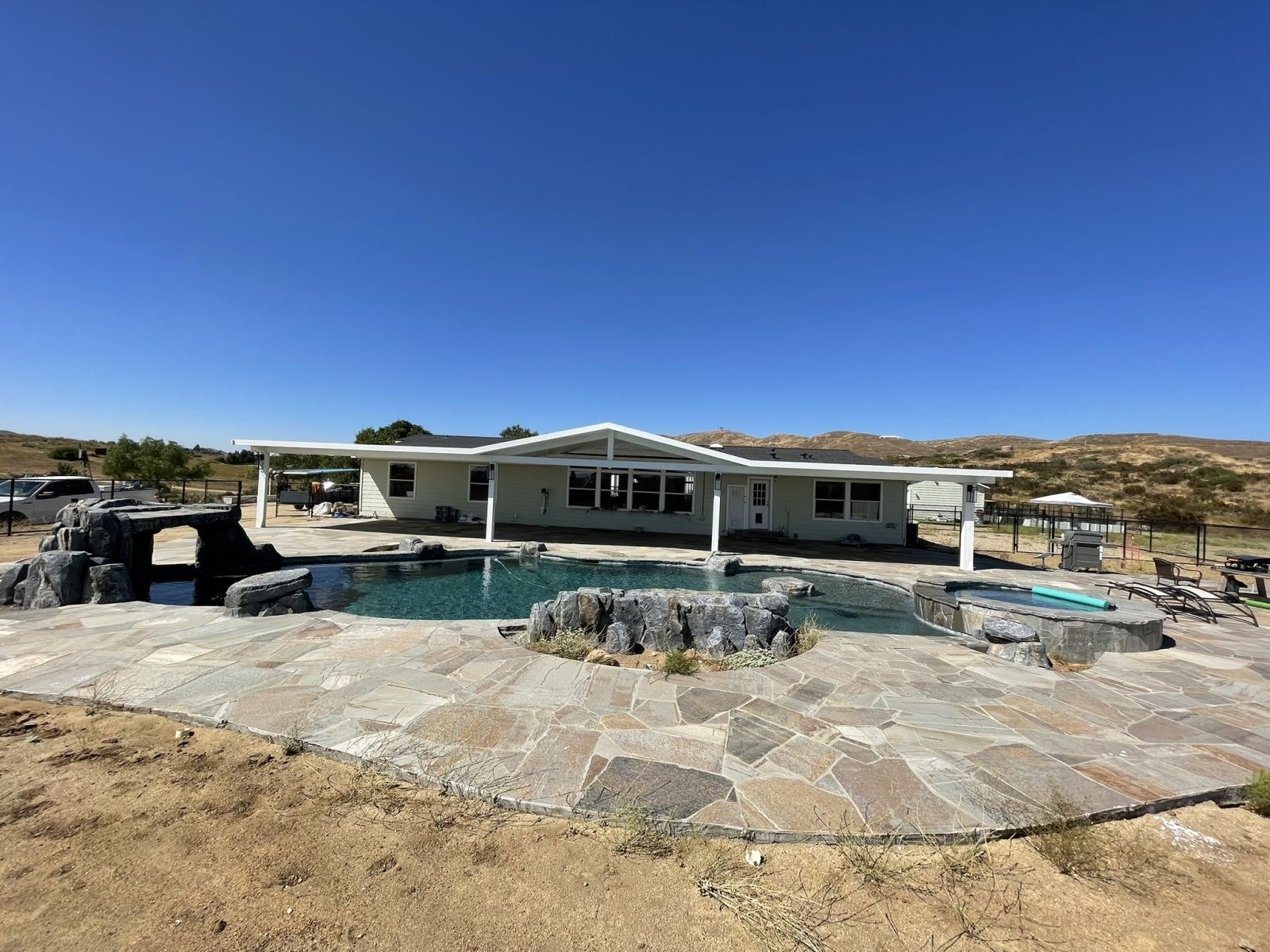 A ranch-style house with a pool and rock features under a clear blue sky.