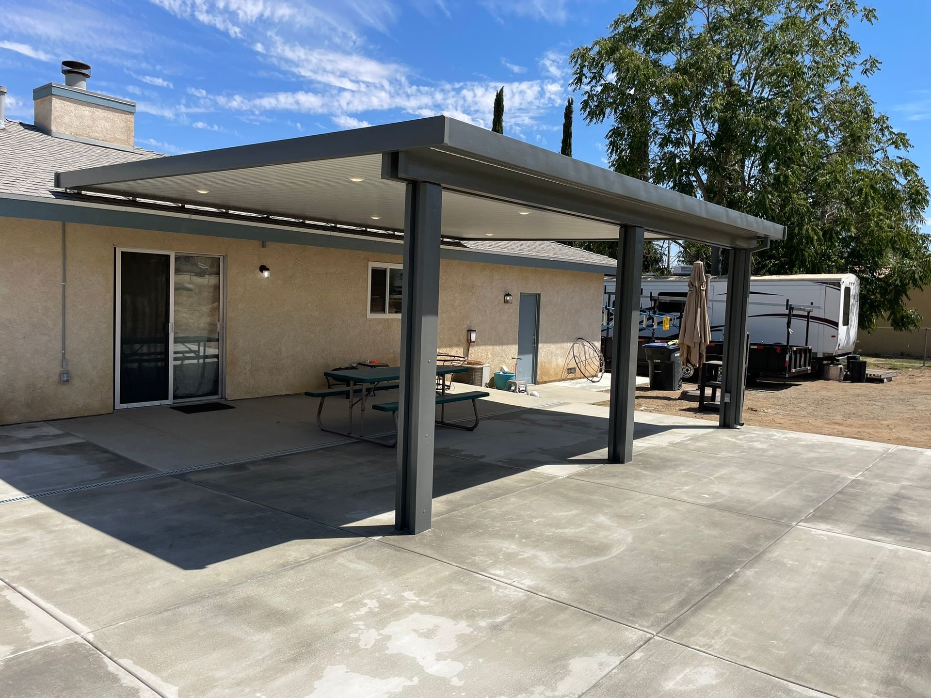 Gray patio cover attached to a beige house, over a concrete patio.