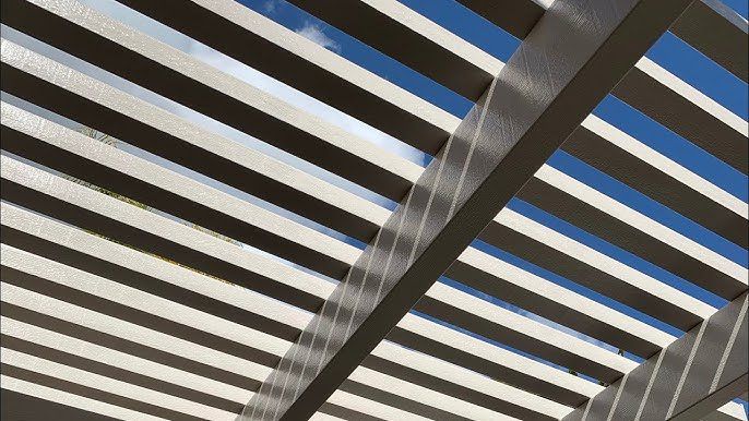 Overhead view of a pergola casting linear shadows against a blue sky.