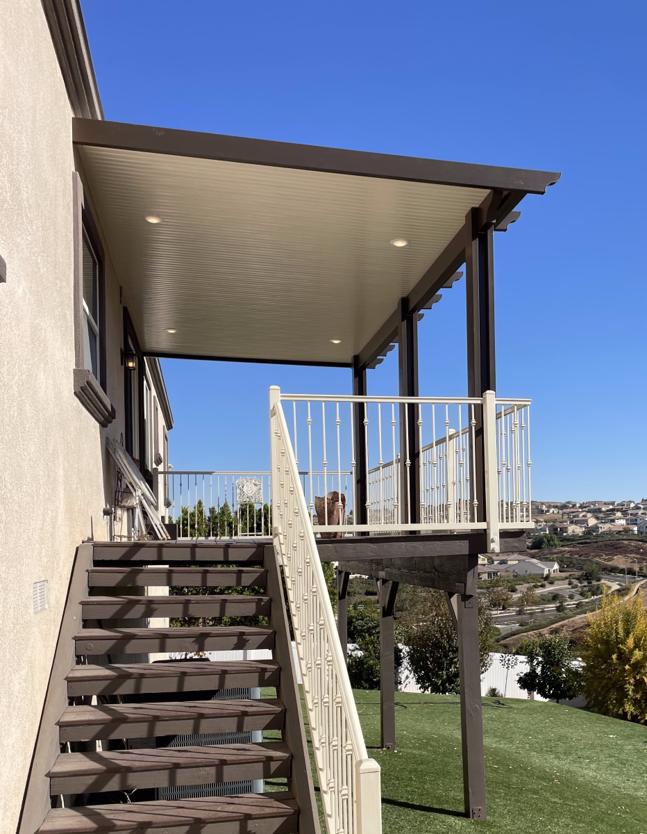 Deck with stairs, covered patio, overlooking a hillside with a bright blue sky.