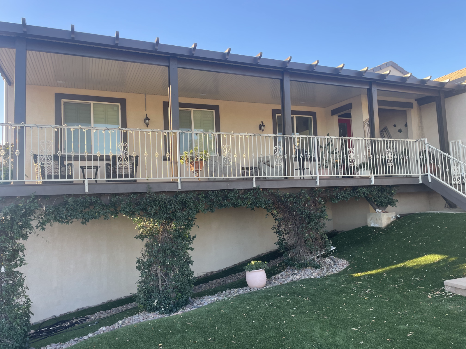 Beige house with a covered deck, white railings, and green ivy growing along the base.
