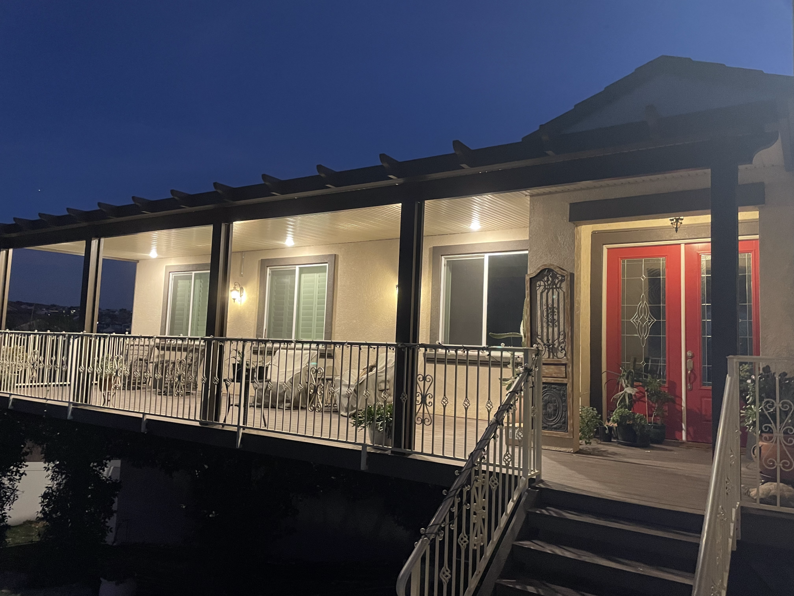 House exterior at dusk with a covered porch, red double doors, and walkway with railings.