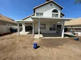 White two-story house with a covered patio, blue sky, and a backyard with brown dirt.