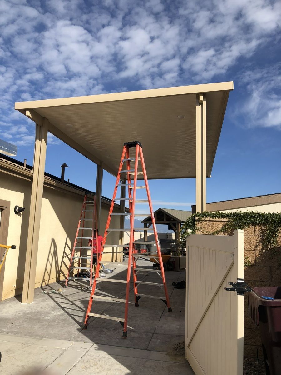 A beige patio cover with two orange ladders, next to a beige building.