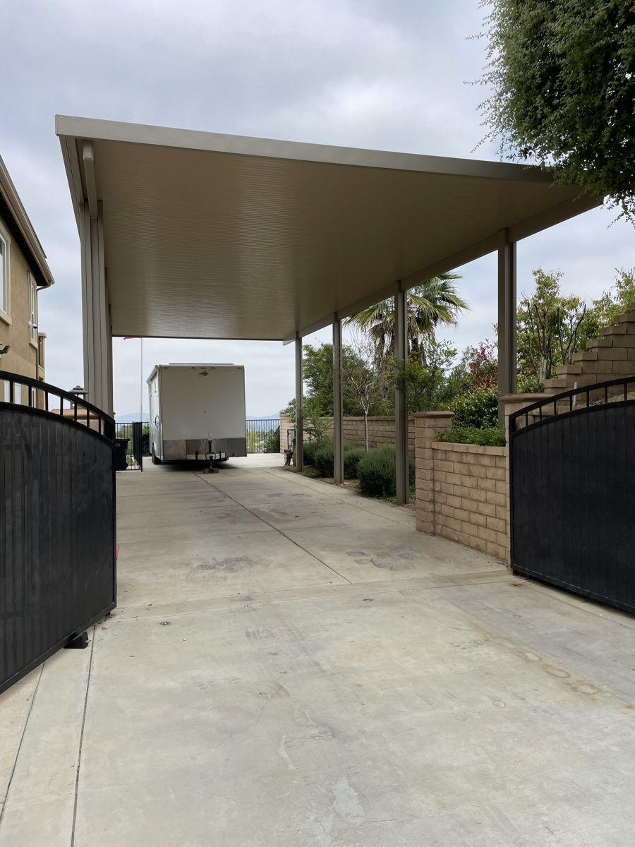 Driveway with black gates, carport, and a delivery truck.
