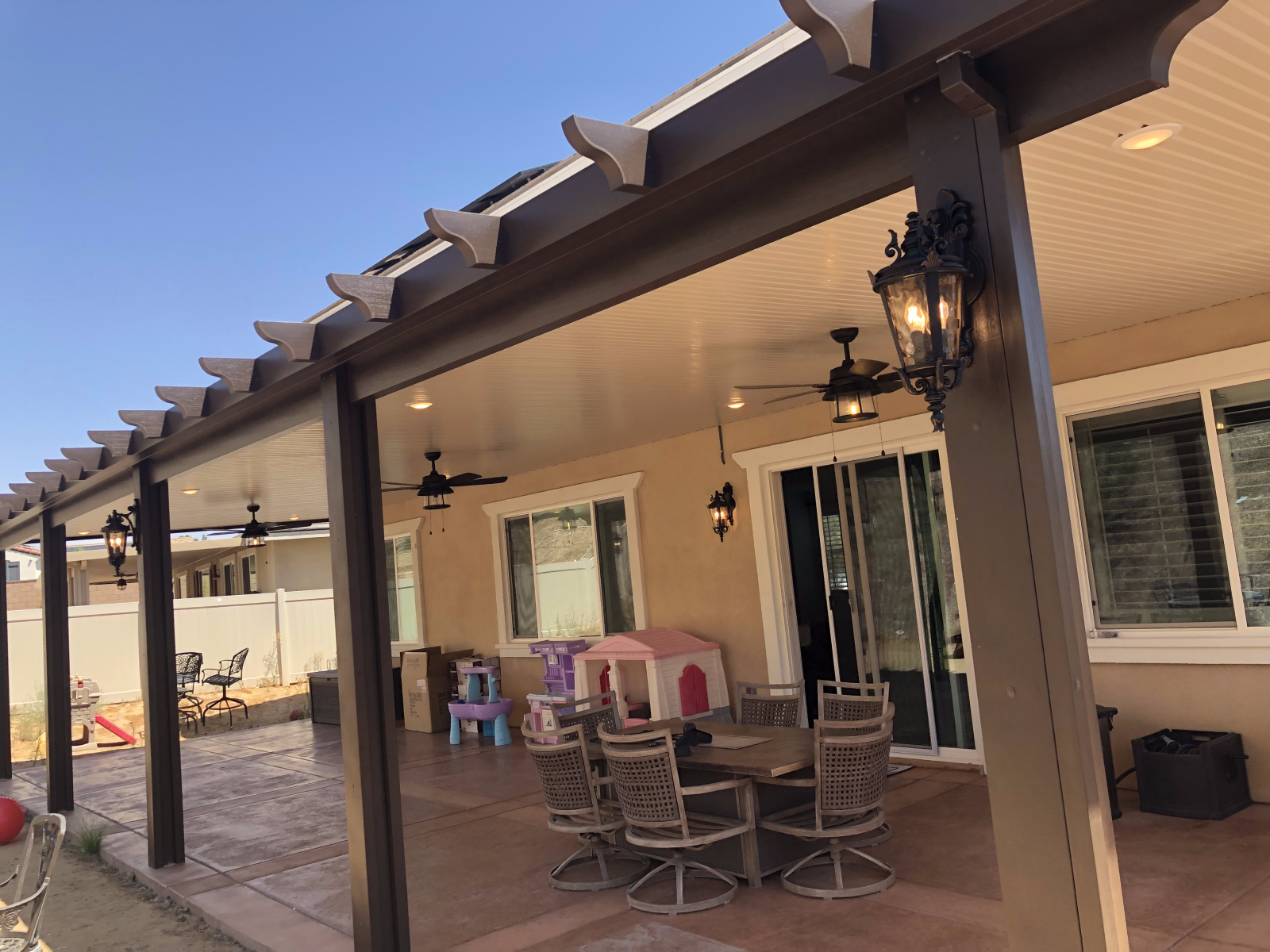 Covered patio with dining set, lights, and a view of the backyard on a sunny day.