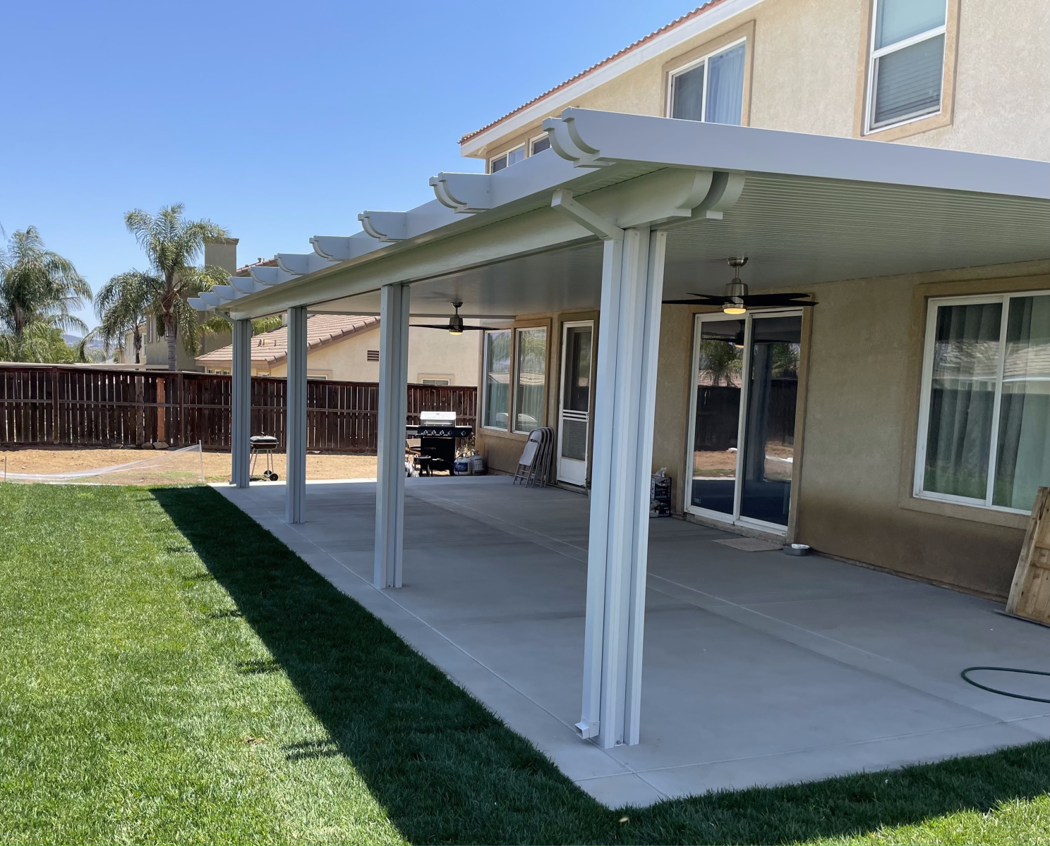 A backyard patio with a gray concrete floor and overhead cover, with a green lawn.
