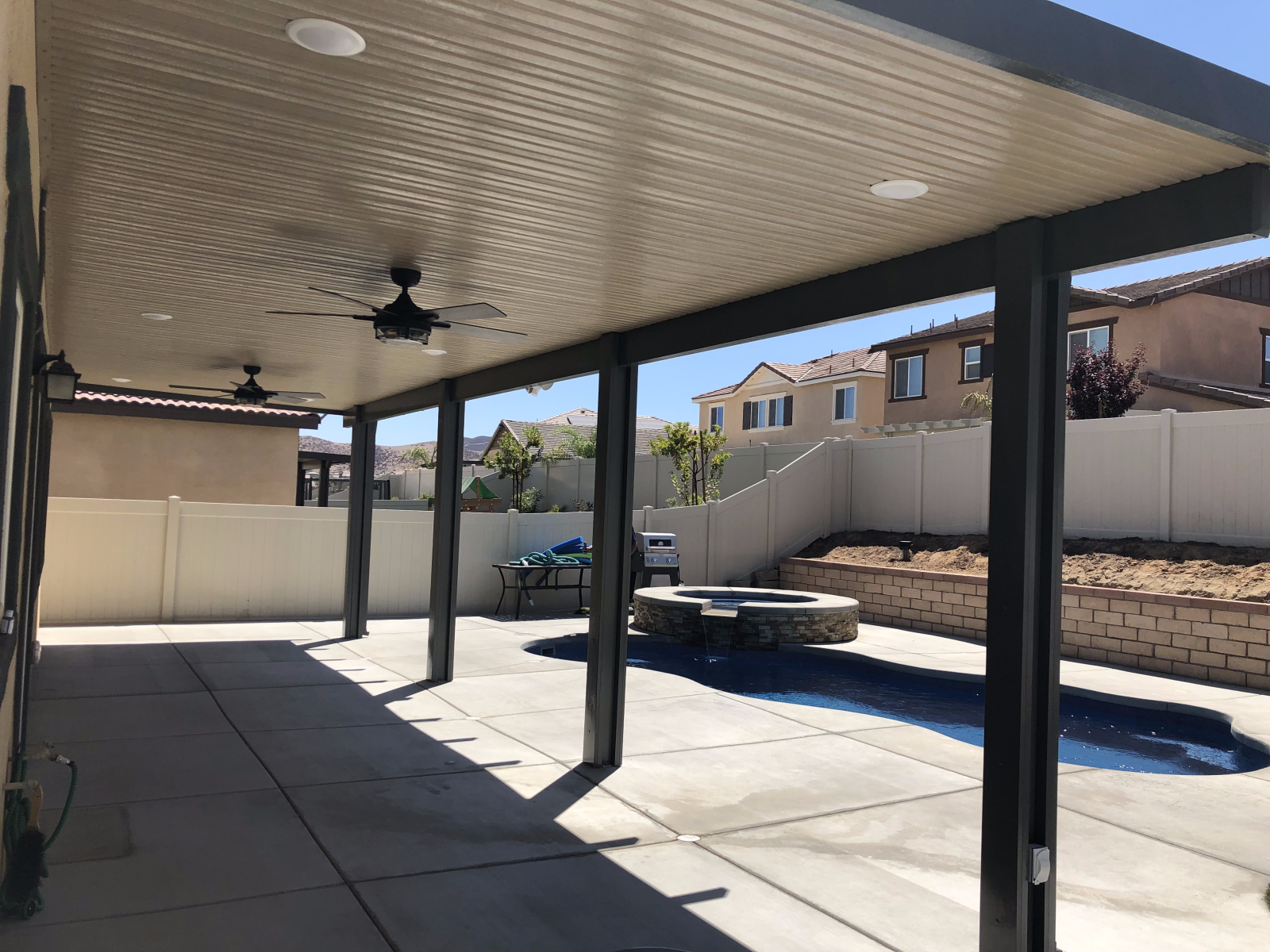 Patio with dark columns, ceiling fans, and concrete floor, overlooking a backyard with a pool.