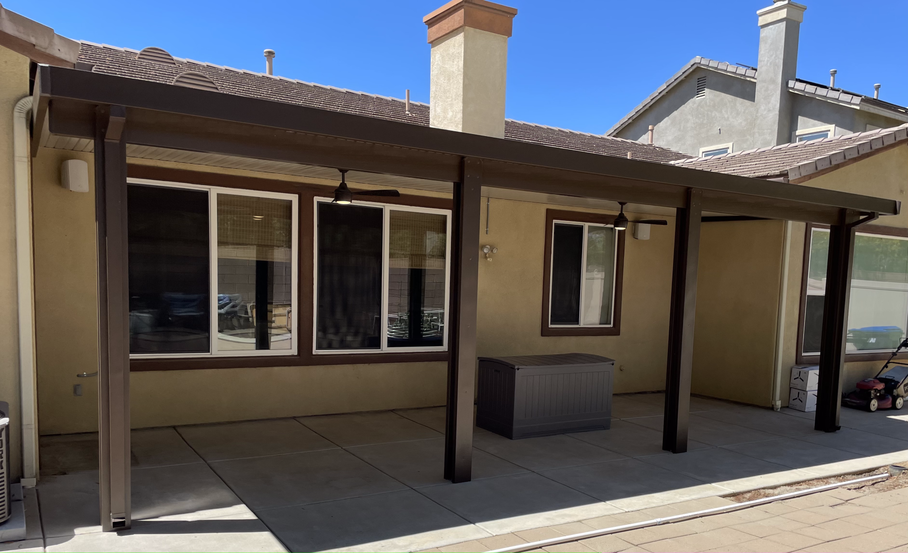 Patio with a brown awning, columns, windows, and a concrete floor.