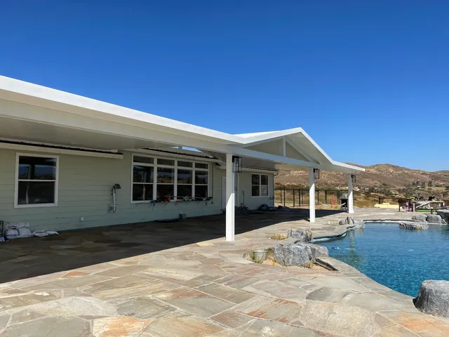 A house with a white roof and columns next to a pool under a bright blue sky.