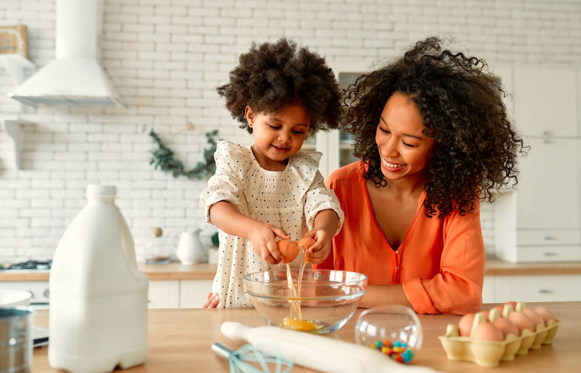 A woman and a little girl are preparing food in a kitchen.