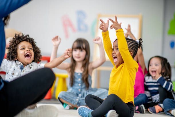 A group of children are sitting on the floor with their hands in the air.