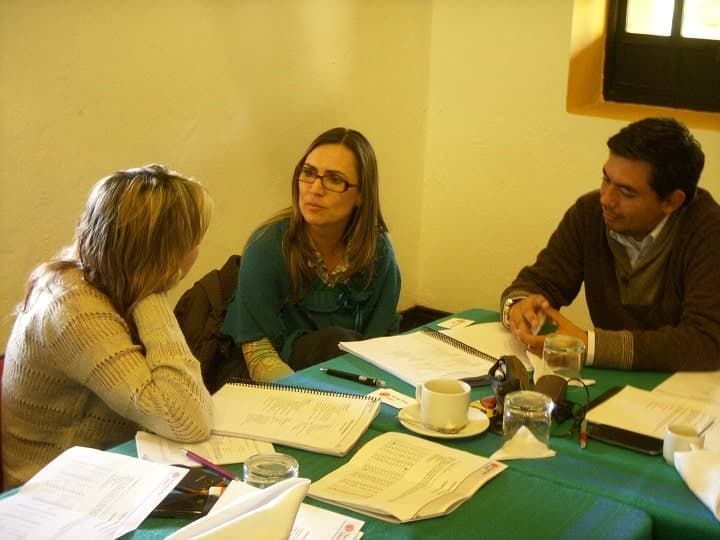 Tres personas están sentadas en una mesa con papeles y una taza de café.