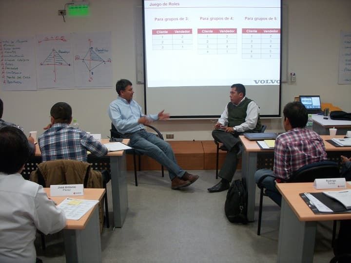 Un grupo de personas sentadas en escritorios frente a una pantalla de proyección que dice Volvo.