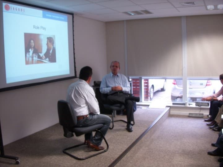 Un grupo de hombres está sentado frente a una pantalla de proyector con una imagen de un hombre en ella.