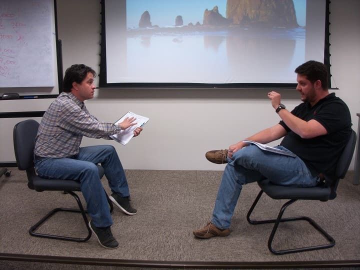 Dos hombres están sentados frente a una pantalla de proyector.