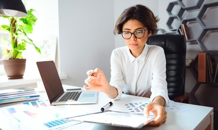 Una mujer está sentada en un escritorio frente a una computadora portátil.