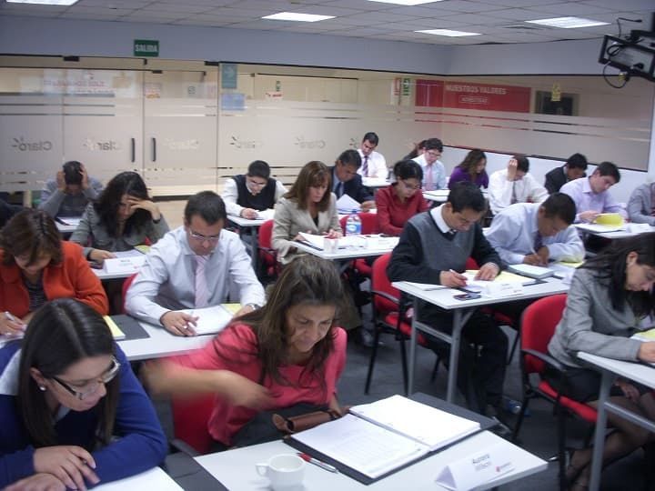 Un grupo de personas están sentadas en escritorios en un aula.