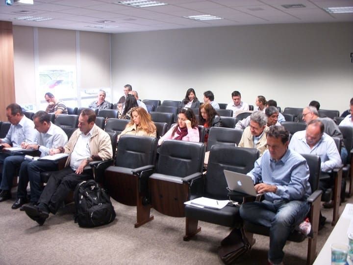 Un grupo de personas está sentado en una sala de conferencias usando computadoras portátiles.