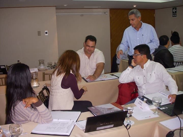 Un grupo de personas están sentadas en mesas con computadoras portátiles.