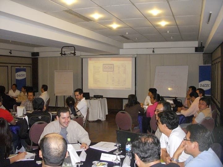 Un grupo de personas está sentado alrededor de una mesa frente a una pantalla de proyector que dice aep