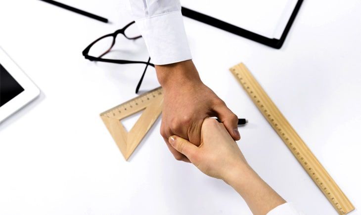 Un hombre y una mujer se dan la mano con una regla sobre la mesa.