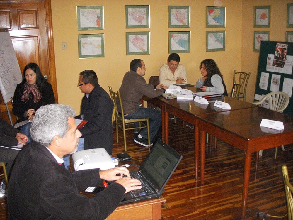 Un grupo de personas está sentado alrededor de una mesa con una computadora portátil.