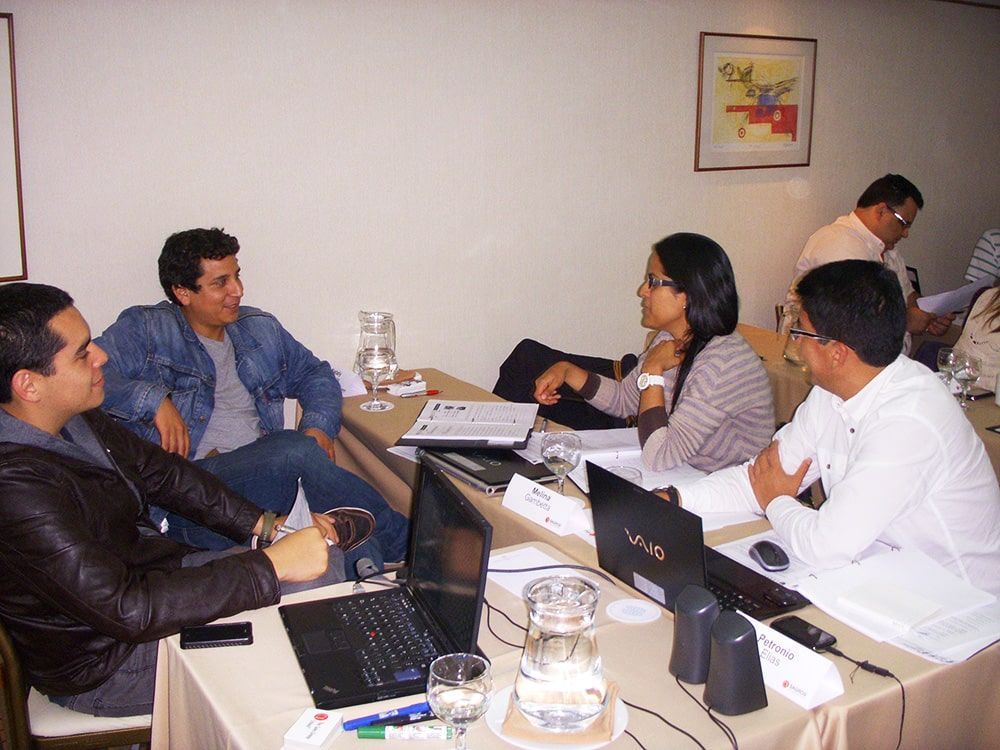 Un grupo de personas están sentadas alrededor de una mesa con computadoras portátiles.