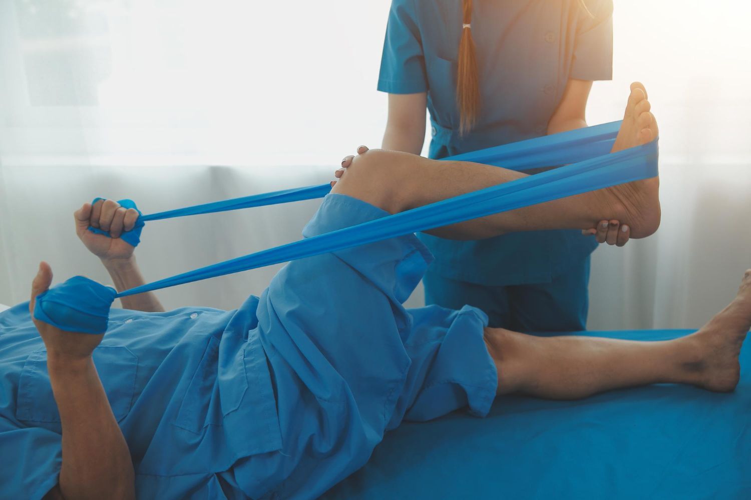 A nurse is stretching a patient 's leg with a resistance band.