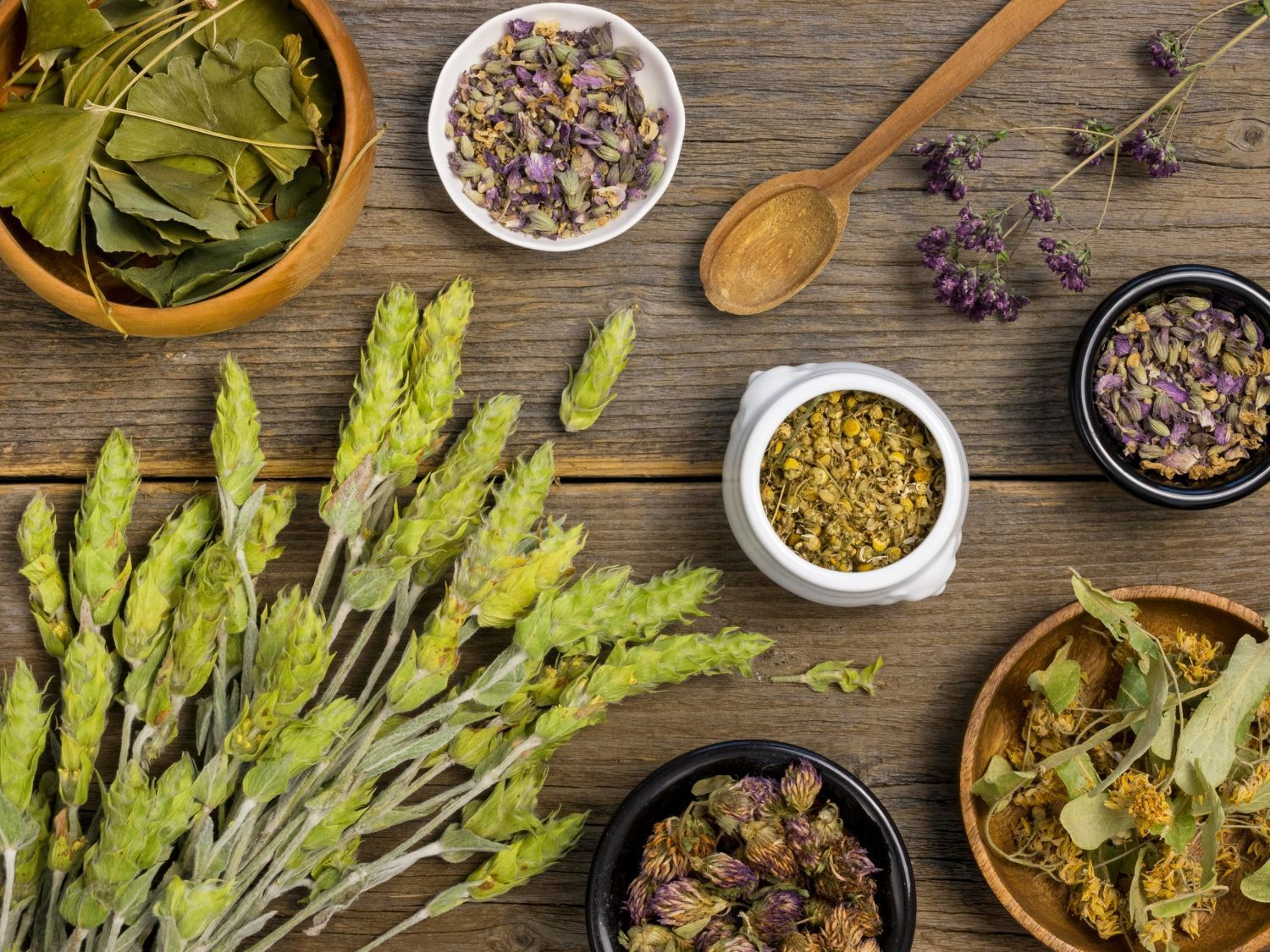 A wooden table topped with bowls of herbs and flowers.