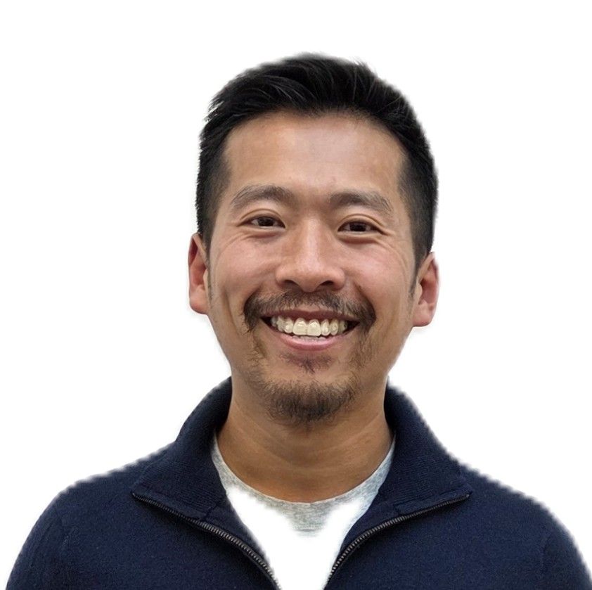 Smiling person with dark hair, wearing a dark blue sweater over a light-colored shirt.