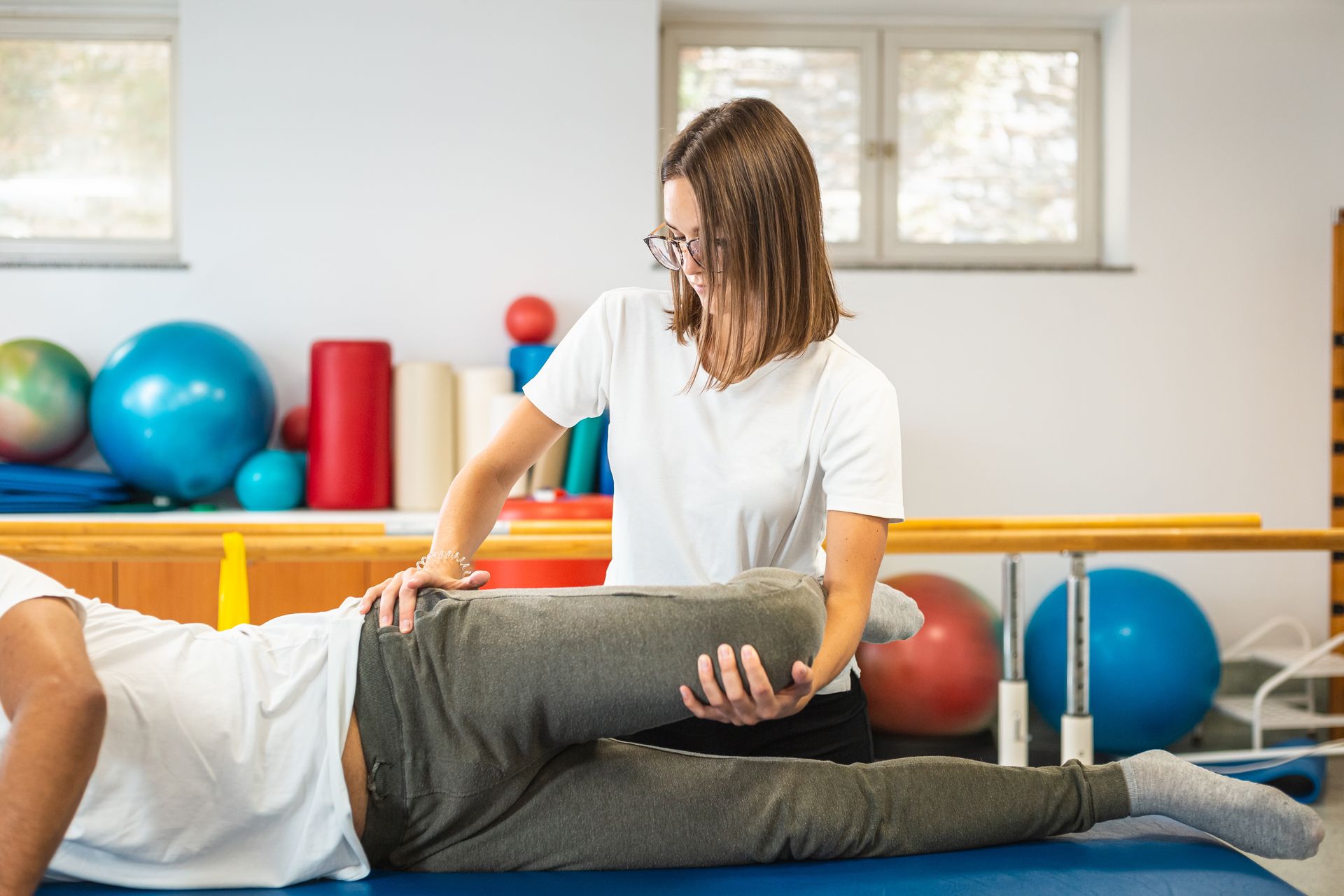 A woman is stretching a man 's leg on a table.