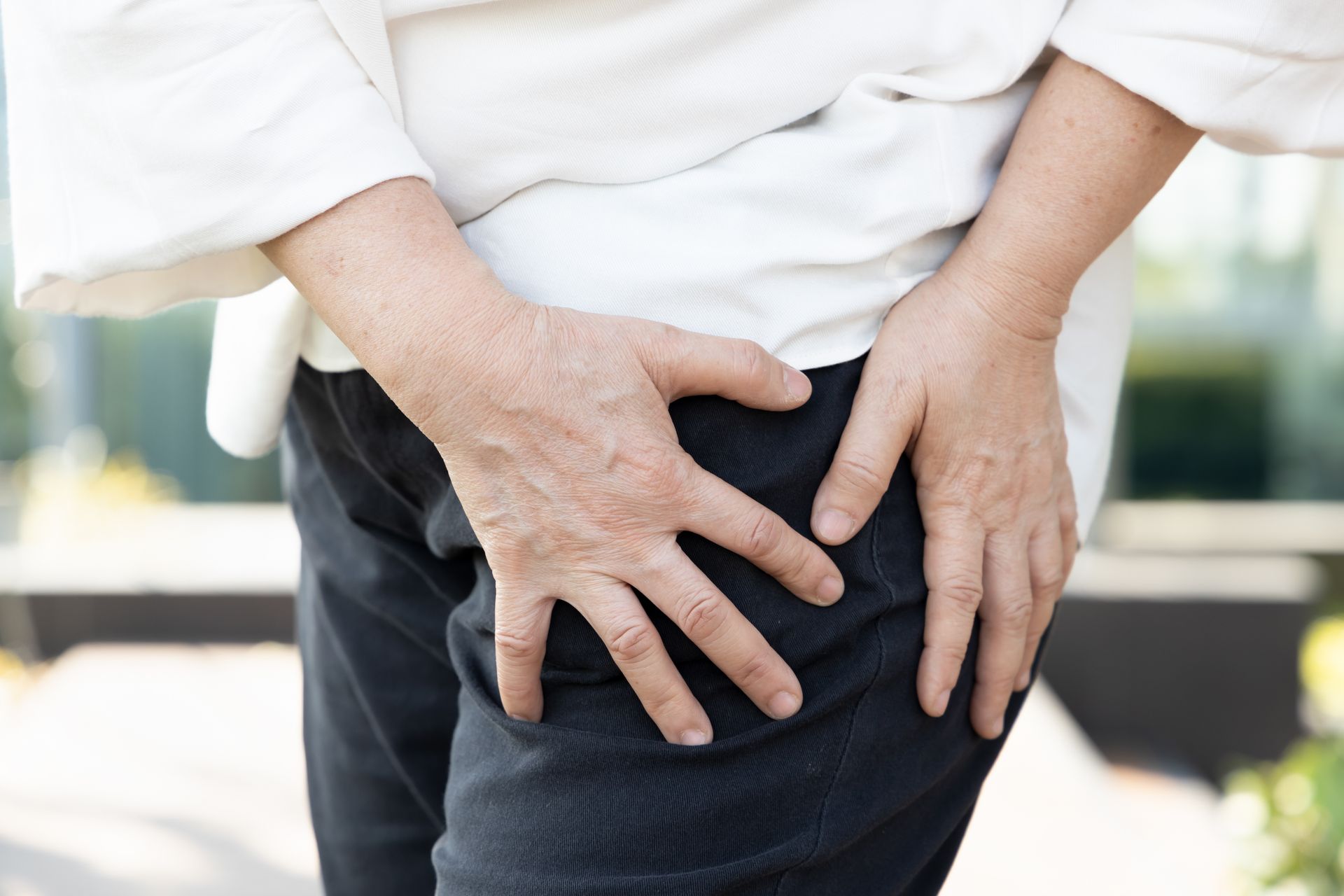 Person holding their hand on their hip, possibly indicating pain. Wearing black pants and a white shirt.