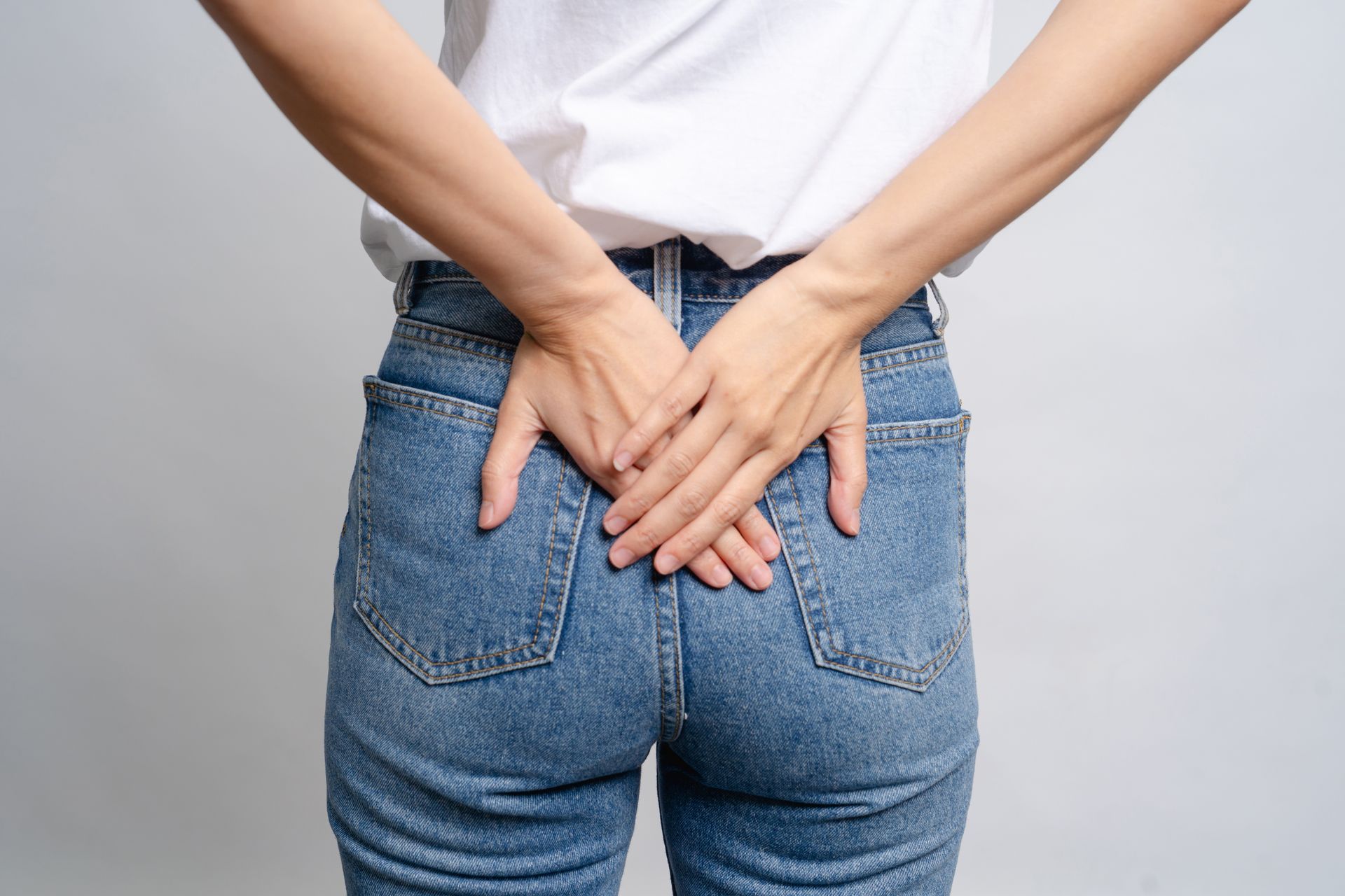 Person in blue jeans with hands crossed behind, possibly indicating back pain.