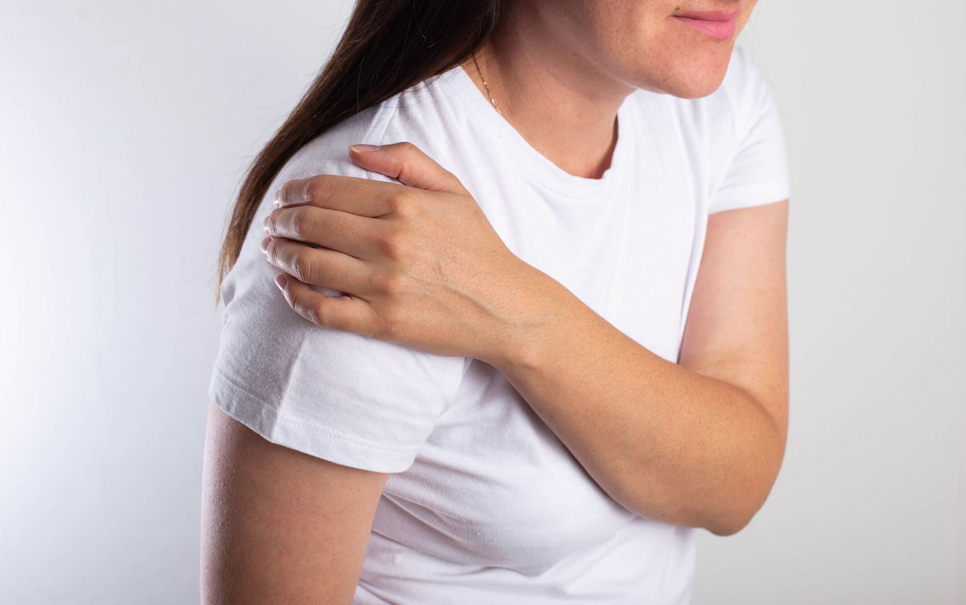 Woman holding her shoulder in pain, wearing a white t-shirt.