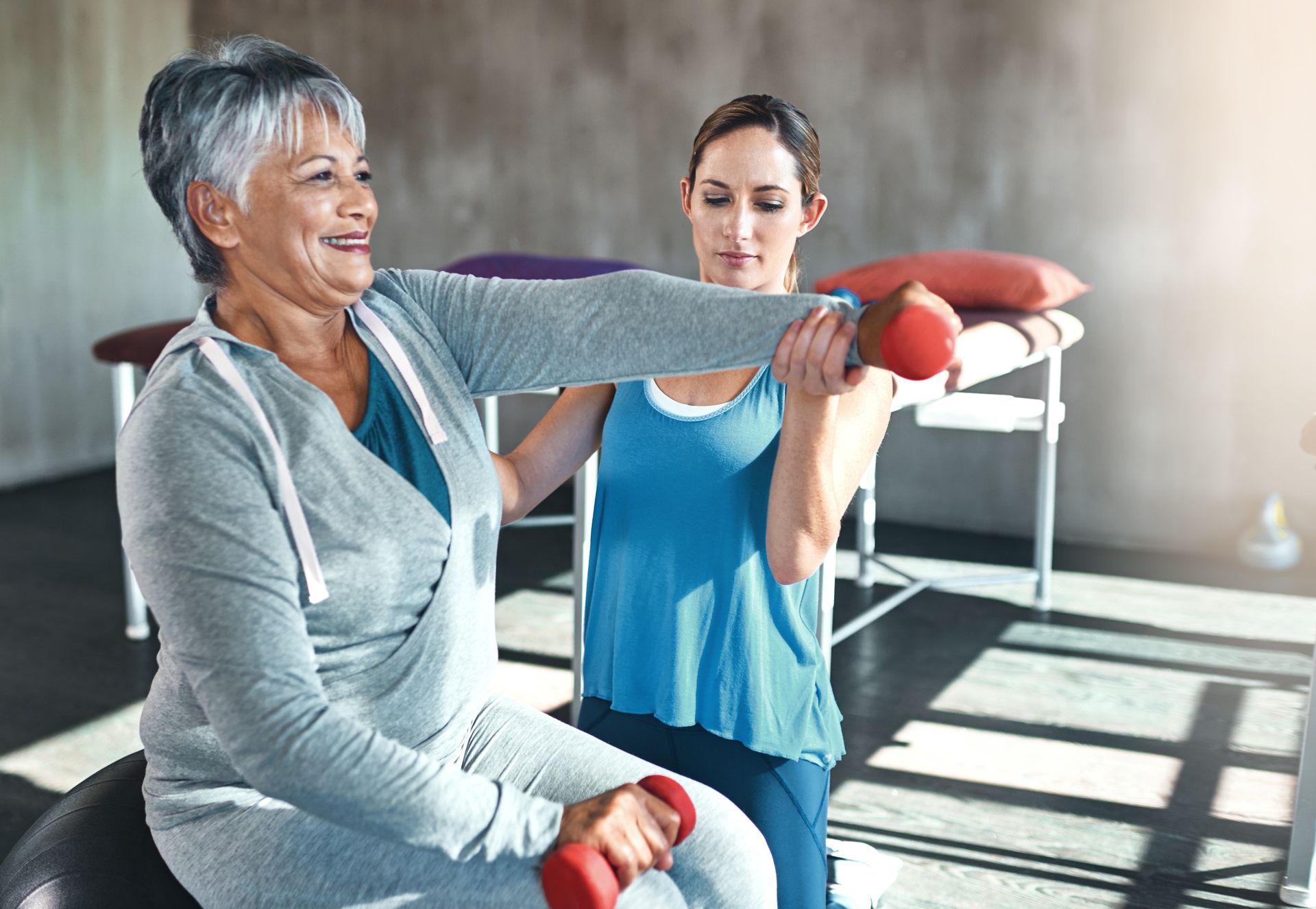 Woman exercising with dumbbell, guided by a trainer in a therapy setting.