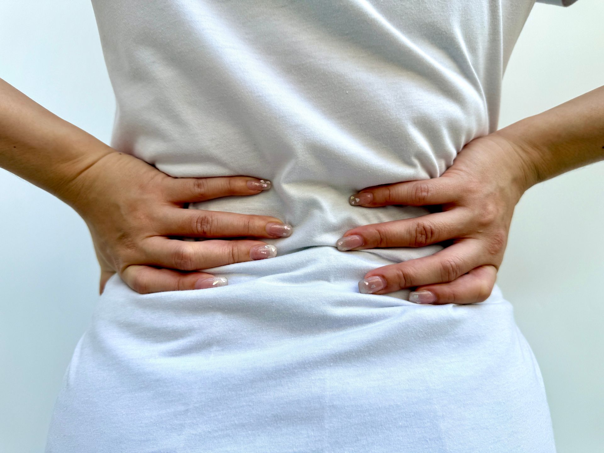 Person in white shirt clutching their lower back, possibly in pain.