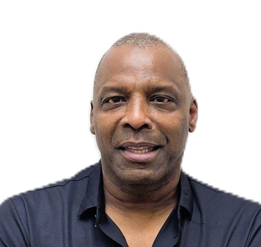 A man wearing a white shirt and a gold watch is standing with his arms crossed.