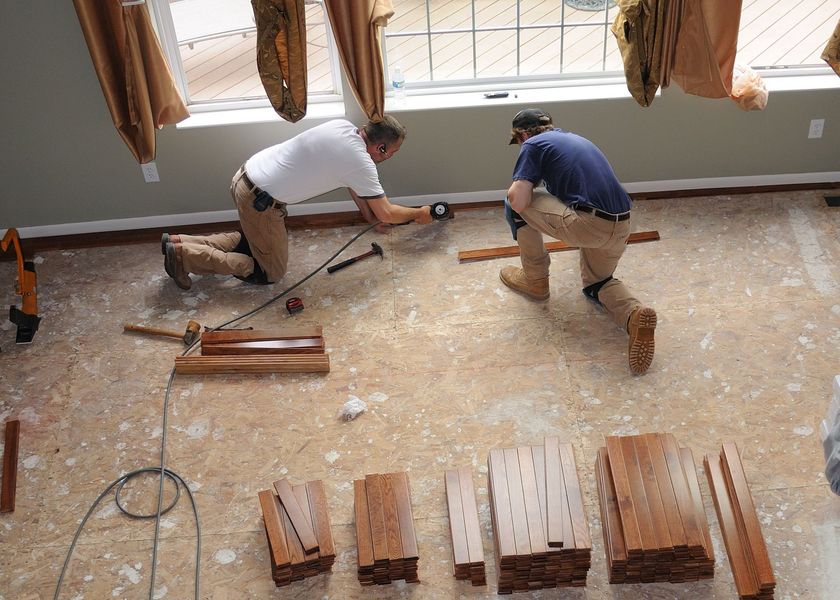 two men are working on a wooden floor in a room