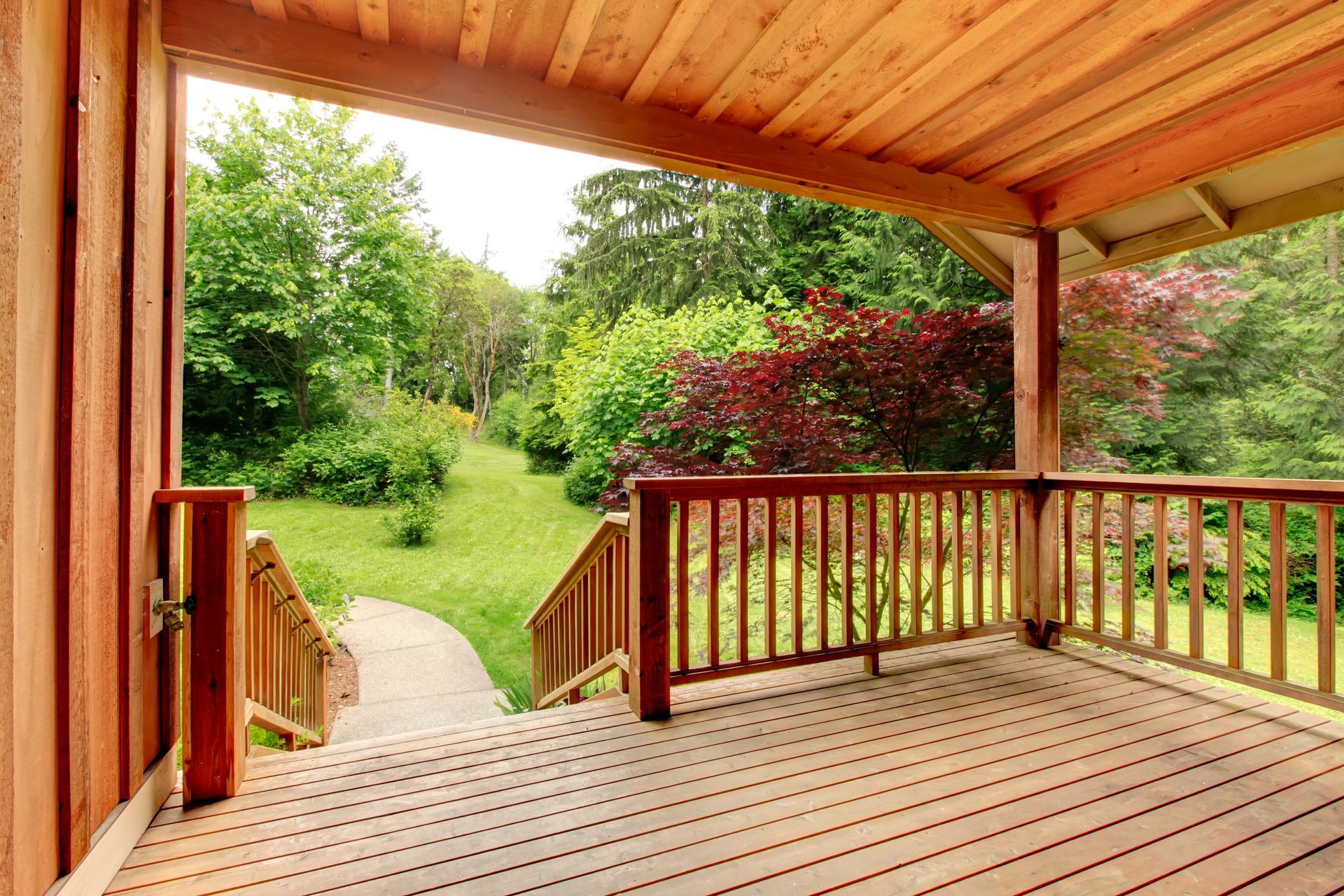 Wooden porch overlooking a green backyard with trees and a garden path