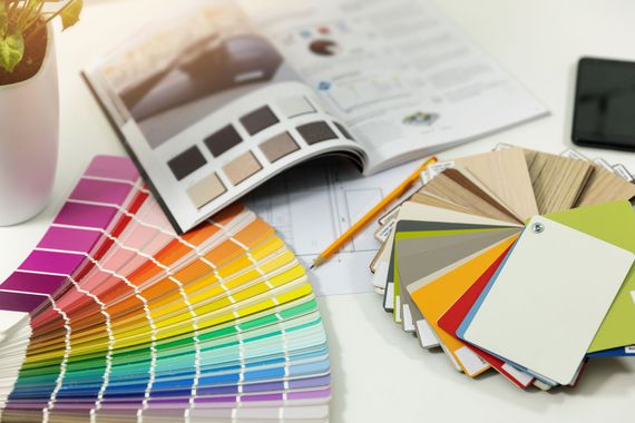 Color swatches and fan decks on a desk beside an open color catalog and pencil