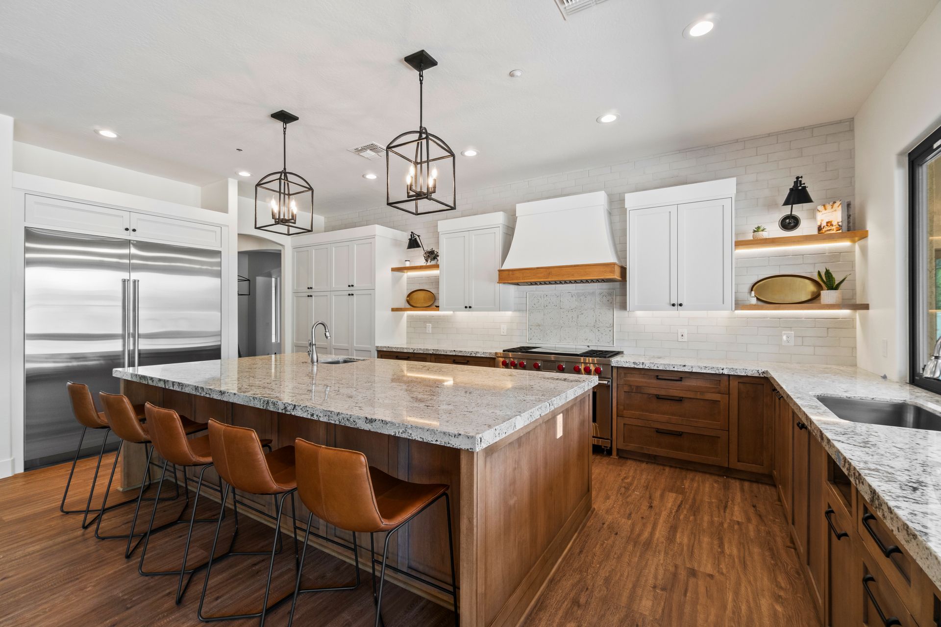 Bright modern kitchen with marble island, white cabinets, wood floors, and two pendant lights