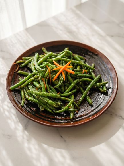 Plate of sautéed green beans garnished with shredded carrots on a dark ceramic dish