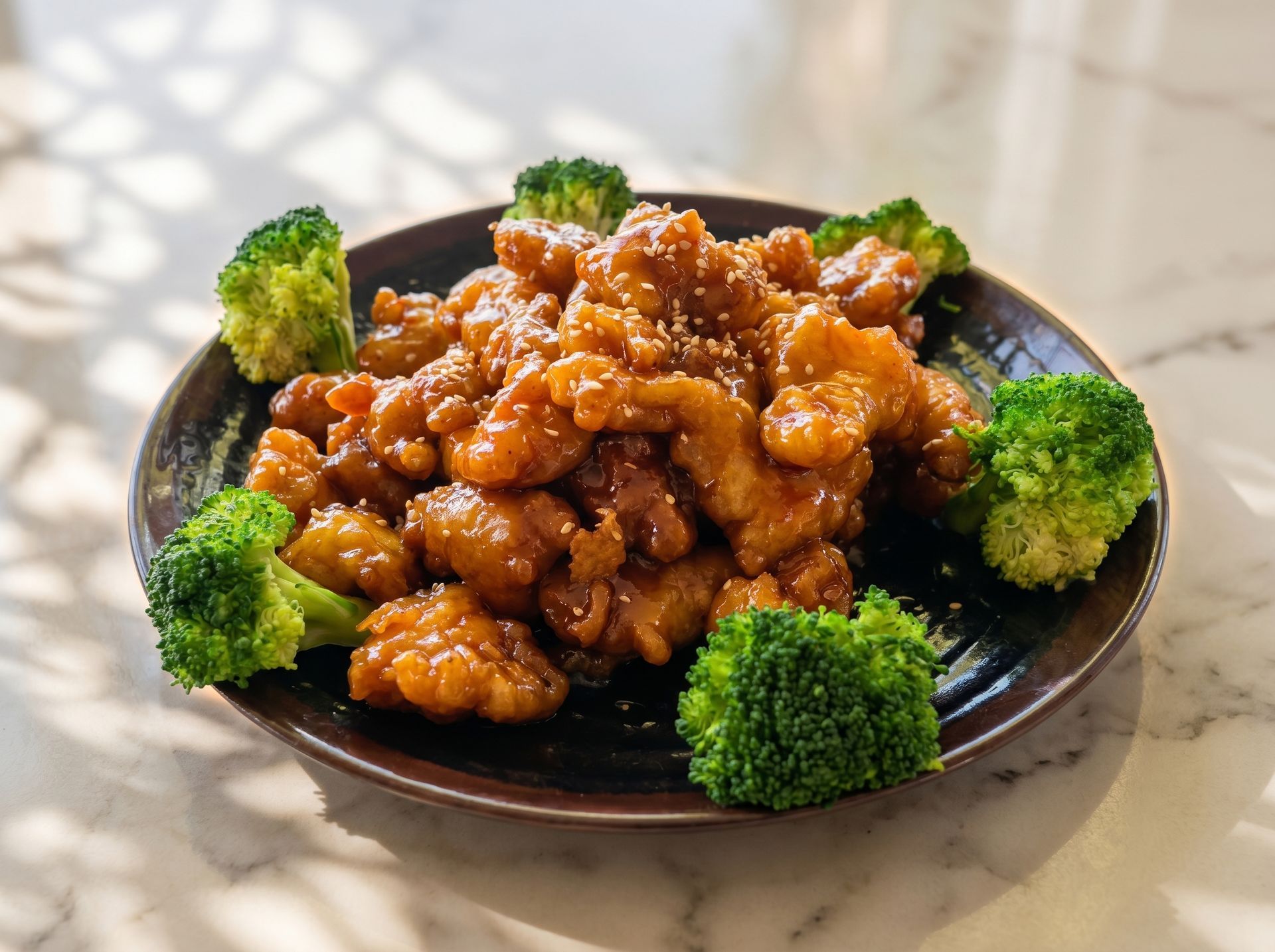Plate of glazed fried chicken pieces garnished with broccoli florets on a marble table